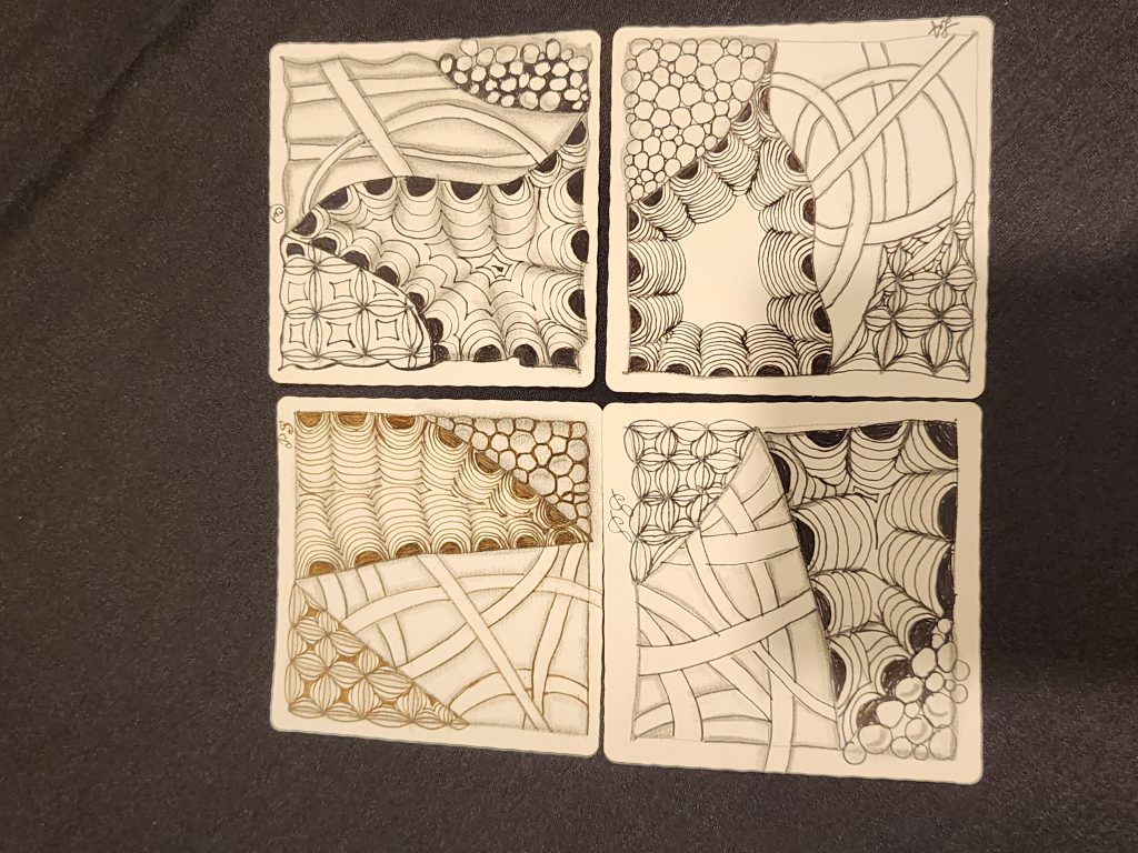 A black tablecloth with 4 square paper sheets. Each paper square was done by a different student, showing their own creative work, and is decorated with 4 different patterned sketches. Crescent Moon, Hollibaugh (overlapping bridges), Bales (decorated grids), and Tipple (bubbles).