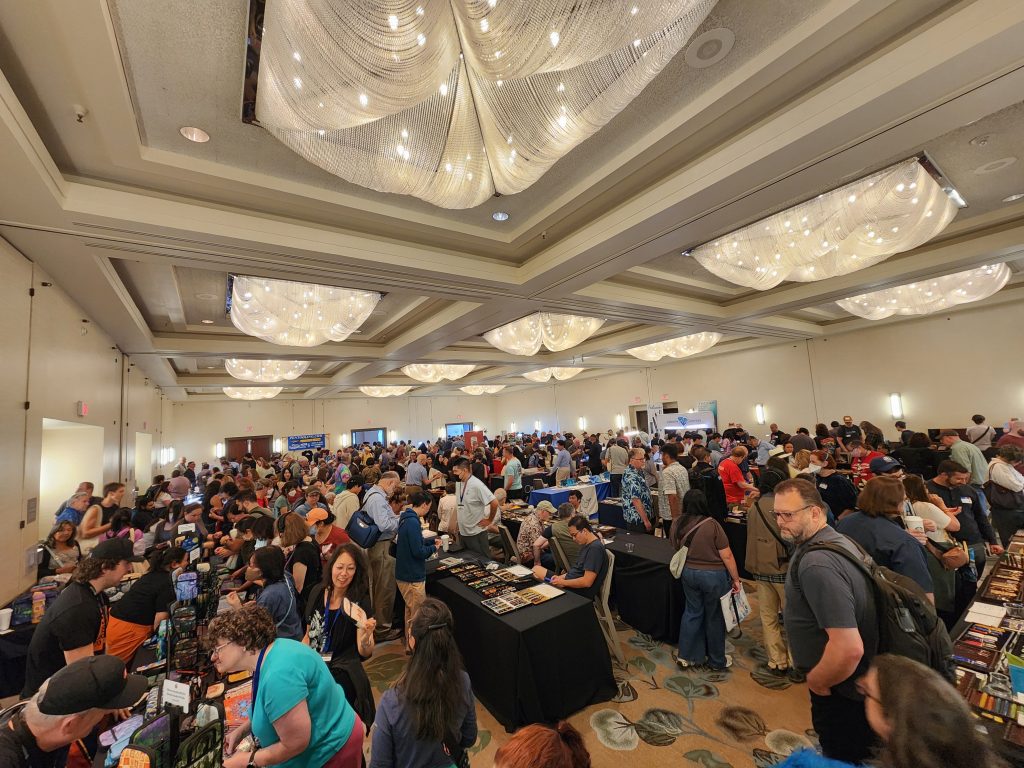 A large hotel ballroom, filled with vendor tables and large crowds of people.