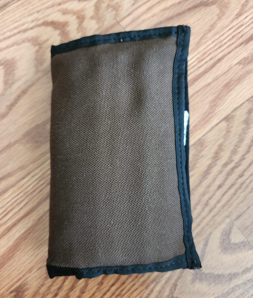 The Nock Co Hightower, a bifold case in coffee brown, constructed with a 1000D nylon material with black border trim. The case is closed, showing only the exterior.