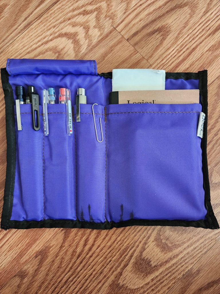 The Nock Co Hightower, a bifold case constructed with a 1000D nylon material with black border trim. The case is open, exposing an amethyst purple interior, 3 pen pockets on the left, a deep notebook pocket on the right.