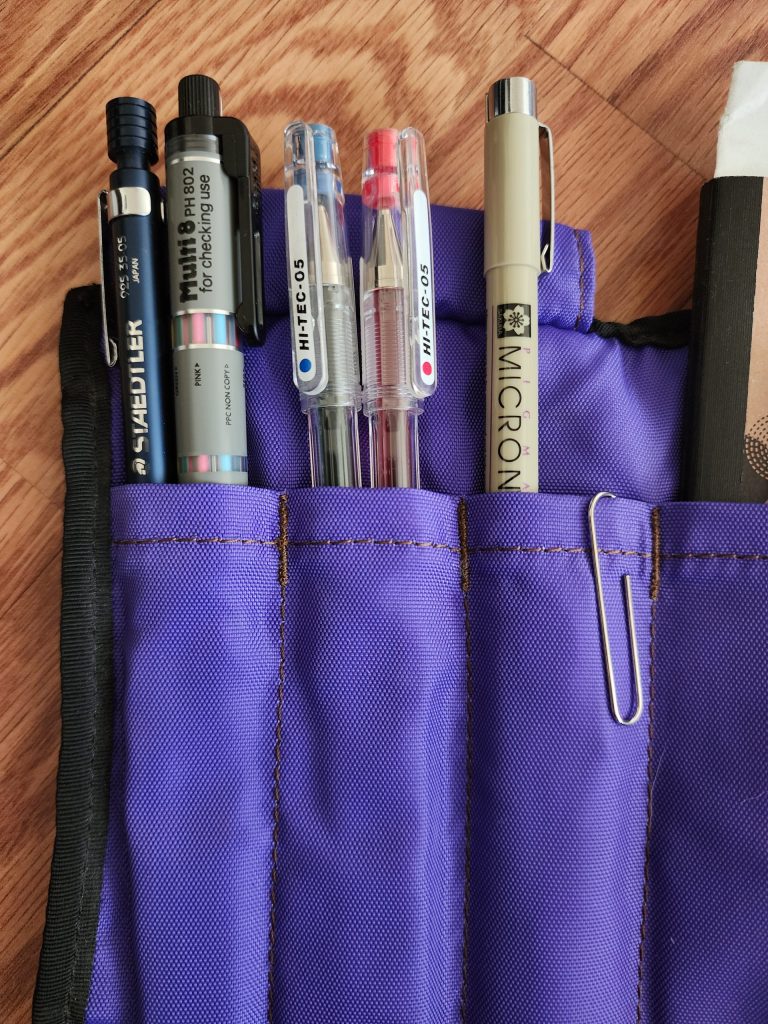 A closeup of the 3 pen pockets of the Nock Co Hightower. An assortment of writing instruments are pulled out of the pockets.