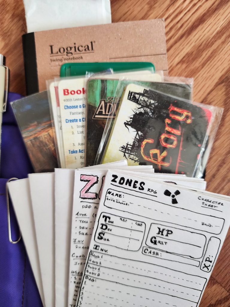 An assortment of papers, pocket size RPG and dungeon crawling games, a notebook, and other miscellany are arranged on top of the Nock Co Hightower, showing how much can fit inside the single pocket side of the case.