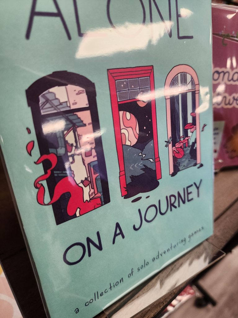 A light blue zine cover depicting 3 open windows, each with a different landscape (part of the buildings in a city, open hills with a moon and planet in view at night, and a forest with various vegetation and insects). The title is "Alone On A Journey, a collection of solo adventuring games"