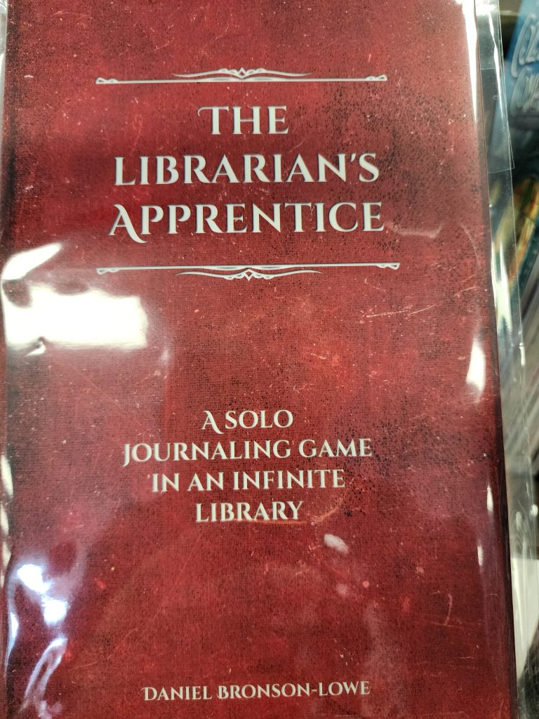 A reddish-brown, leather looking booklet cover reads, "The Librarians Apprentice, A solo journaling game in an infinite library".