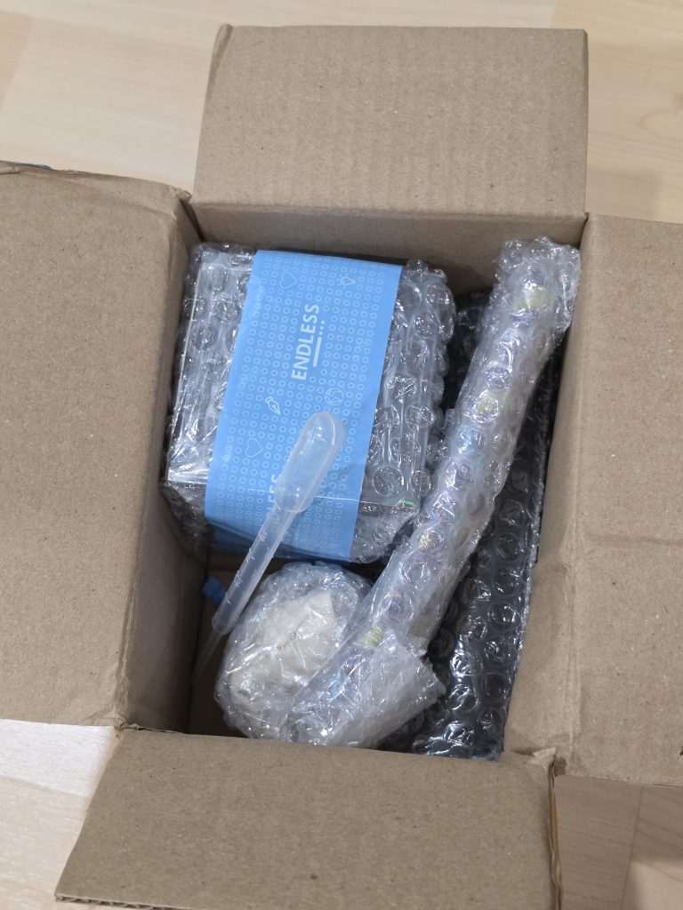 A small cardboard box with several bubble wrapped items inside, the only hints are a single pipette and blue tape that says "Endless".